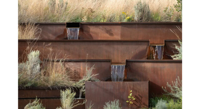 A narrow channel of water moves through layered steel forms, eventually reaching the pond below. Native aspens and dryland grasses flank the runnel, offering dappled shade, texture, and rhythm to the courtyard’s carefully restrained design.